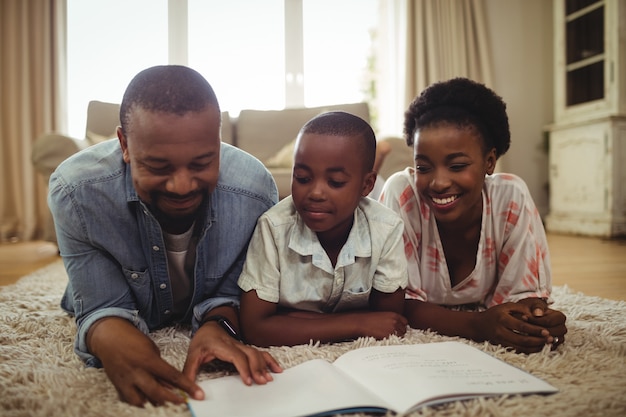 Genitori e figlio che leggono un libro mentre giacciono su un tappeto