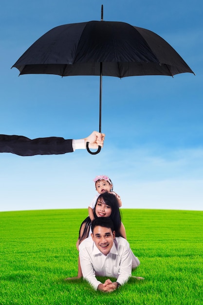 Foto genitori e il loro bambino sdraiati sull'erba sotto l'ombrello