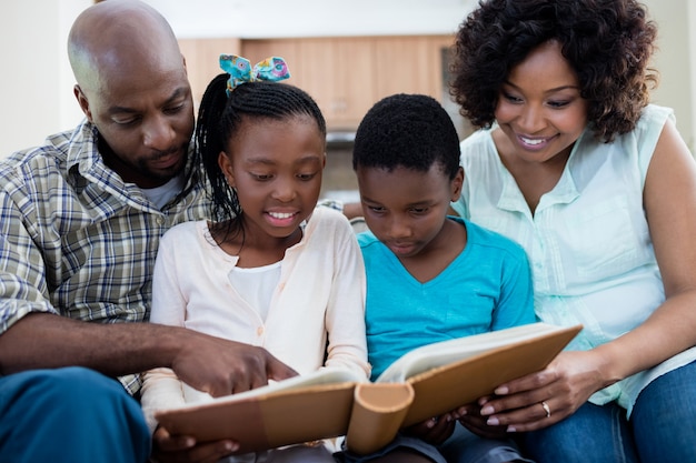 Parents and their children looking at photo album in living room