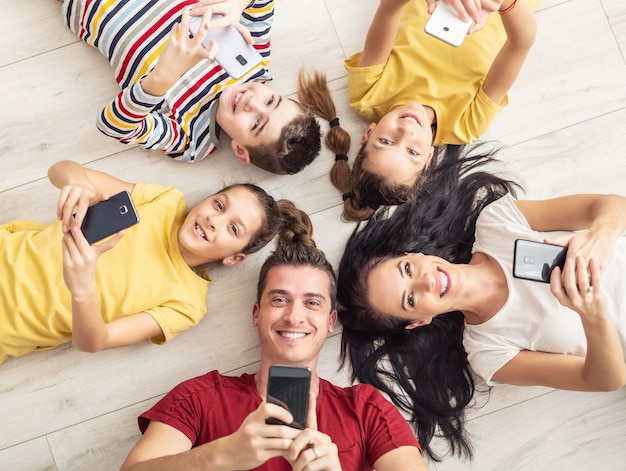 Parents and three children all hold mobile phones in their hands looking up.