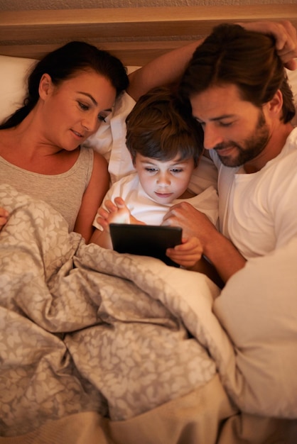 Photo parents watch and boy with tablet in bedroom for movie digital and educational for learning of child family love and technology with connection to internet for bonding mom and dad relax with son