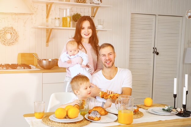 Parents with baby and funny boy smiling and while enjoying buns and juice for breakfast together.