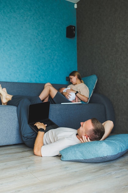 Parents with baby sitting on sofa at home with laptop and talking online A young family with a child works on a laptop at home while sitting on the sofa