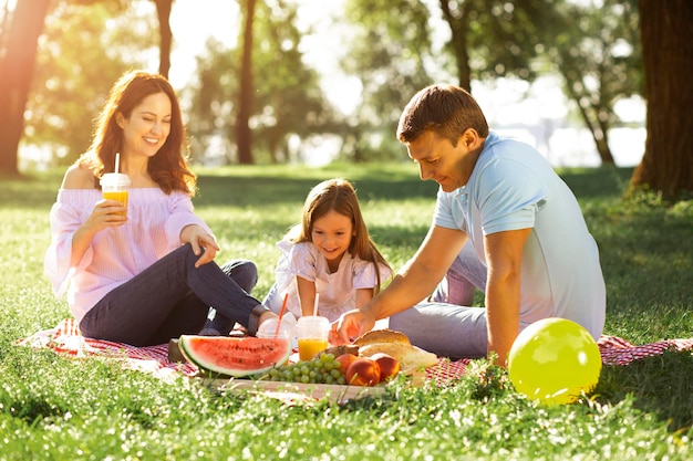 公園でピクニックで果物を食べる娘を持つ親
