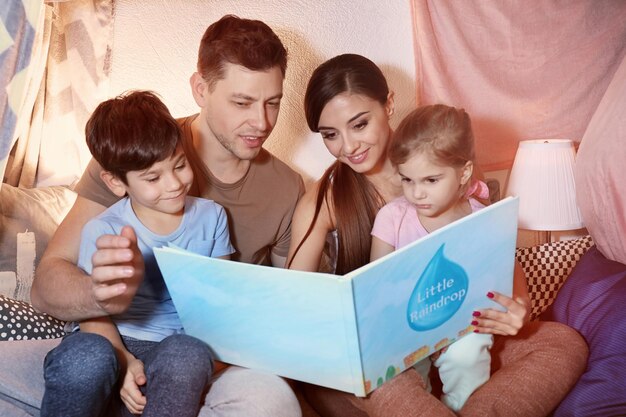 Foto genitori con bambini piccoli che leggono la storia della buonanotte nel tugurio di casa