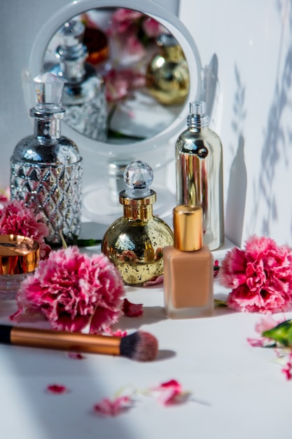 Parfum, foundationcrème, penseel en reflectie met dianthusbloemen op witte muur. make-up concept