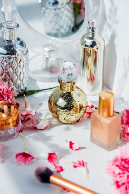 Parfum, foundationcrème, penseel en reflectie met dianthusbloemen op witte muur. make-up concept