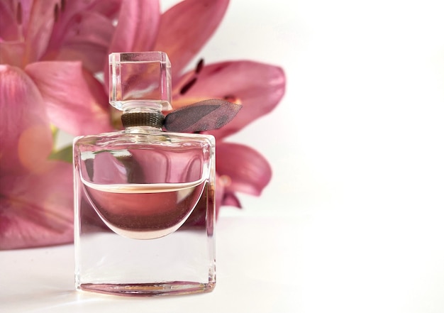 Parfum with flowers on white background. A perfume bottle surrounded by lilies petals in pink and white color. Eau de toilette, eau de parfum, beauty concept.