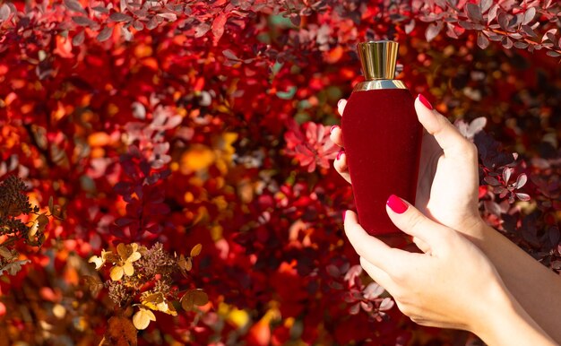 Parfumflesje in de hand met parfumflesje op herfstachtergrond met schoonheidsproduct