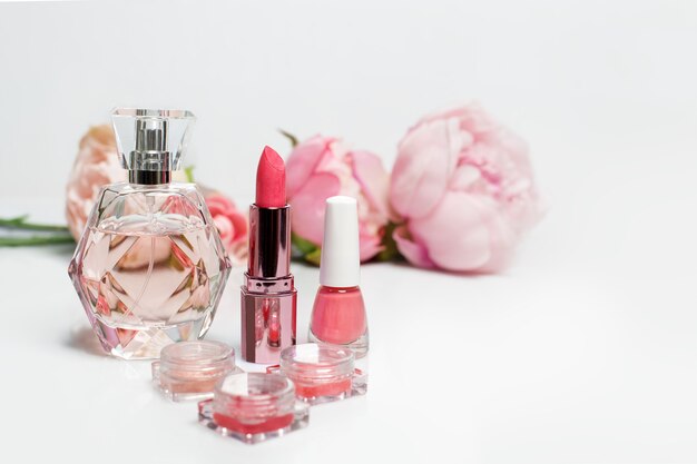 Parfumflesje, nagellak, lippenstift en bloemen op wit oppervlak