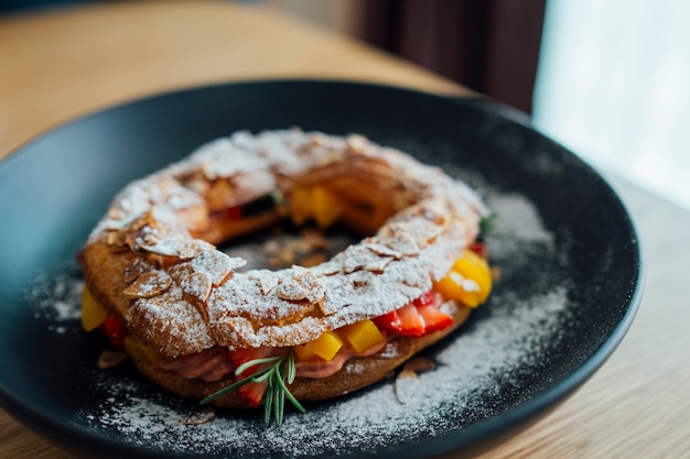 Парижский брест, фаршированный персиками и клубникой в ​​черной тарелке