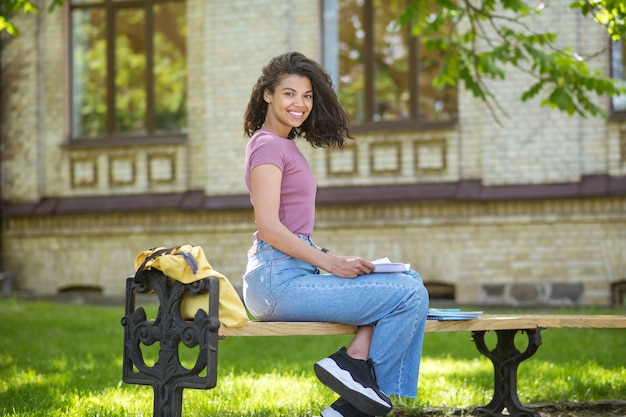 In the park. A girl in a pink tshirt holding sitting on the bench in the park