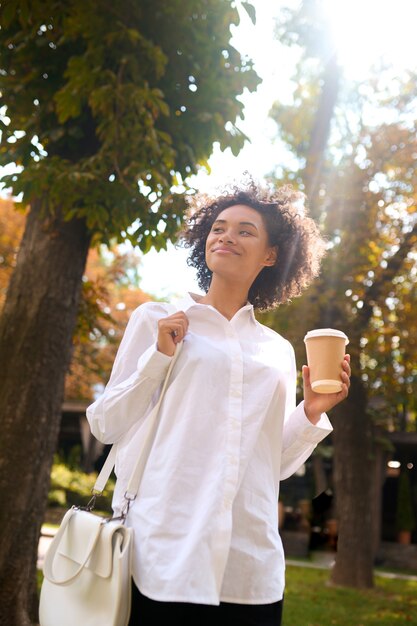 In the park. A girl in a white shirt with a coffee cup in the park