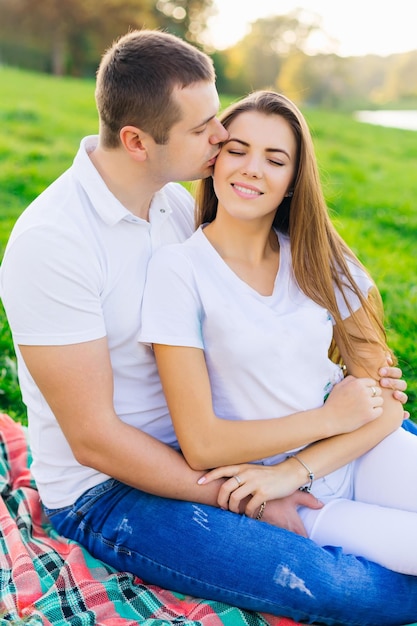 푸른 잔디 위의 공원에서 귀여운 다정한 커플이 한 남자가 여자에게 부드럽게 키스하고 있다