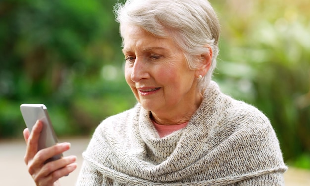 Park lezen en senior vrouw met smartphone kennisgeving en online communicatie met technologie Texting sociale media voor virtuele netwerken of internet zoeken browsen of bericht op app