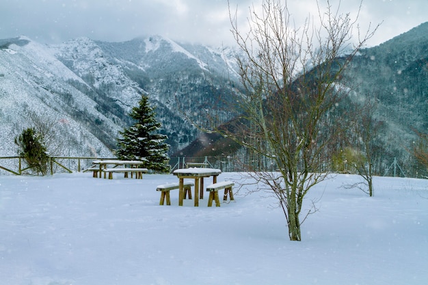 Park without people in mountain viewpoint in winter day with spectacular views to the bottom of snowy mountains wooden benches and tables covered by thick layer of snow