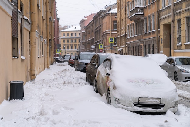 Parked cars covered with snow on an uncleaned snowy road after snowfall. Bad winter weather, increased precipitation and snow levels concept.