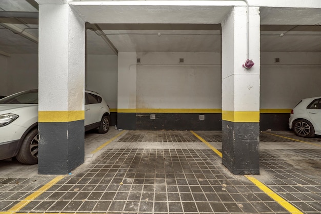 Parking spaces delimited with yellow paint on the ground floor of a building with a garage and parked vehicles