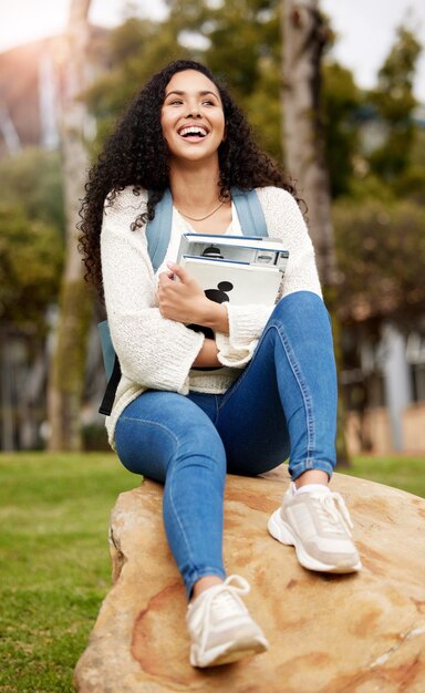 Foto parkuniversiteit en vrouw met boek op de campus om kennis te leren en te studeren op rots onderwijsschool en gelukkige vrouwelijke student lachen met leerboek voor informatieonderzoek of universiteitsles