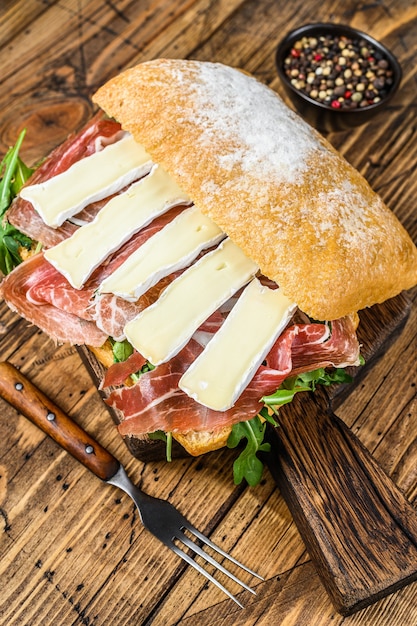 Parma Ham Sandwich on ciabatta bread with arugula and camembert brie cheese. wooden table. Top view.