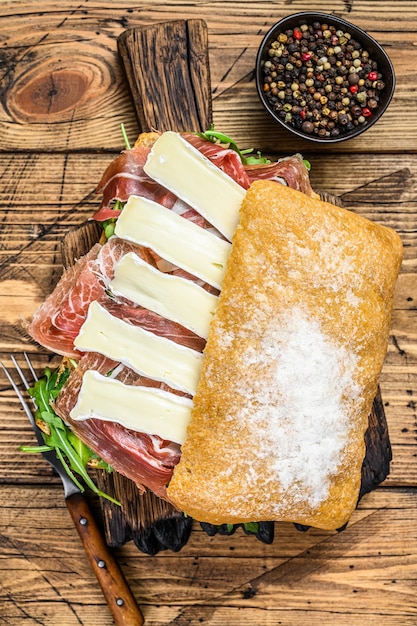 Parma Ham Sandwich on ciabatta bread with arugula and camembert brie cheese. wooden table. Top view.