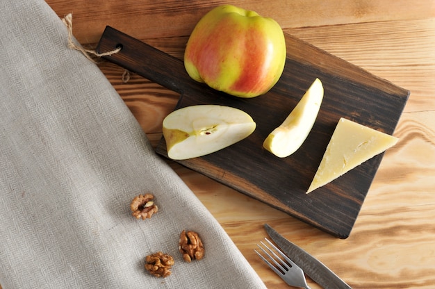 Сыр пармезан и яблоко на доске и очищенные грецкие орехи