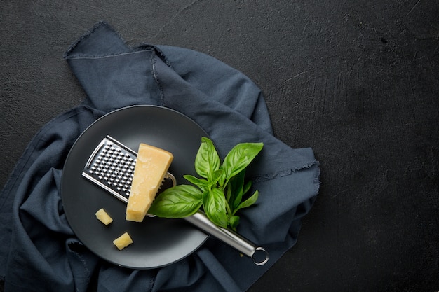 Parmesan cheese, grater and basil on a black