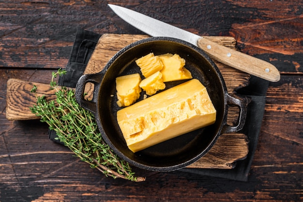 Parmesan hard cheese piece in a pan. Dark Wooden background. Top view.