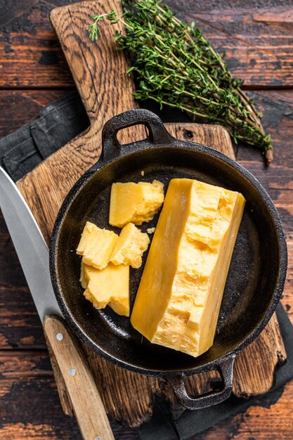 Parmesan hard cheese piece in a pan. Dark Wooden background. Top view.