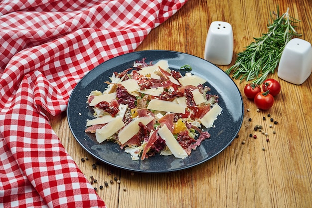 Parmesan, orange, lettuce and jamon salad in black plate on wood.