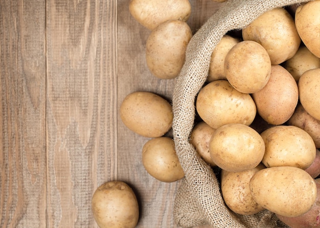 Part of bag with potatoes on wooden background top view