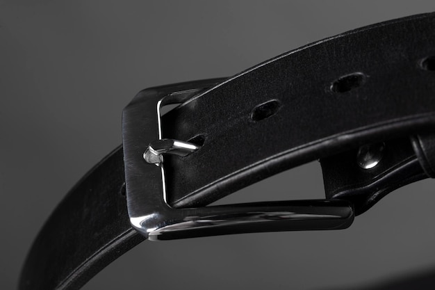 Part of a black leather belt with a metal buckle closeup on a gray background