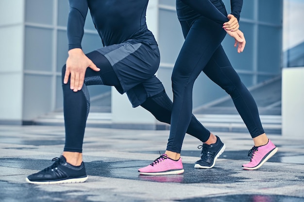 Part of the body of athletic couple is stretching over modern building background.