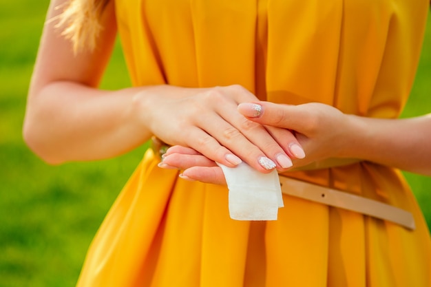 Parte del corpo di una giovane donna in un vestito giallo nel parco. ragazza che usa salviettine umidificate il sudore sul braccio.