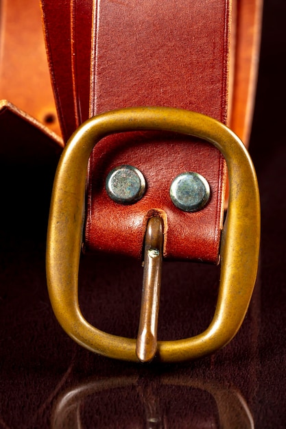 Part of a brown leather belt with a buckle on a dark background