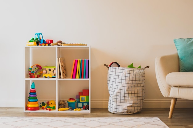 part of children's bedroom white shelf with colorful toys and books cosy armchair near bag with toys comfortable space for children