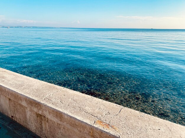 Part of concrete promenade along the clean mediterranean sea under azure sky visible pebbles in the water background wallpaper