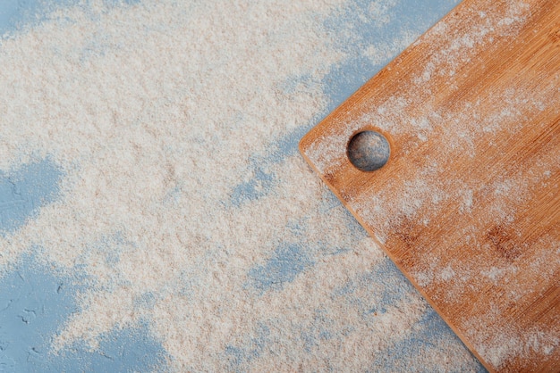 Part of a cutting wooden board on a blue background with flour