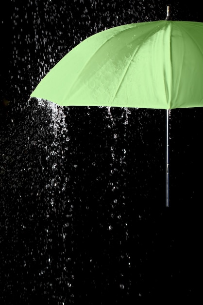 Photo part of green umbrella under raindrops with black background. business and fashion concept.