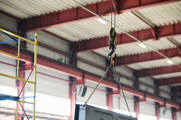 Part of industrial crane with metal hook passing large panel or solar battery