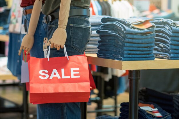 Photo part of male mannequin dressed in casual clothes holding the sales paper shopping bag in the shoppin