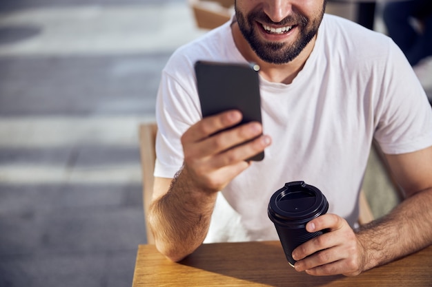 コーヒーを飲みながらカフェのテーブルに座り、スマートフォンを見ている男性の顔の一部をクローズアップ