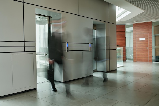 Part of spacious corridor inside office center and two blurred men by elevators