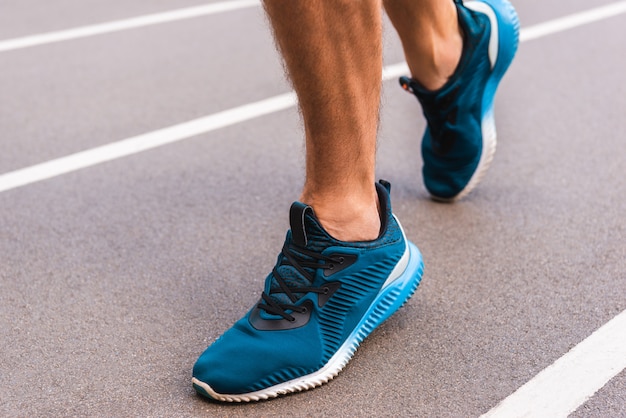 partial view of athletic young sportsman in sneakers jogging on running track