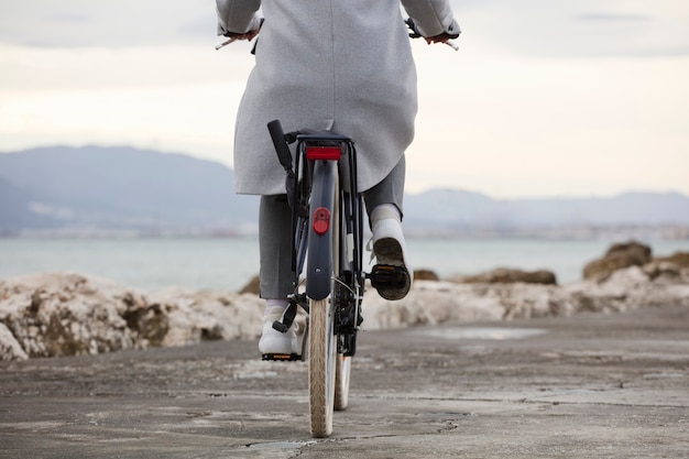 Vista parziale della bicicletta con donna, vestiti grigi, spiaggia sullo sfondo. (focus sulla ruota della bicicletta)