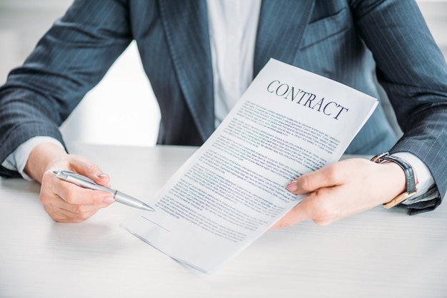 Partial view of businesswoman sitting at workplace and pointing at contract