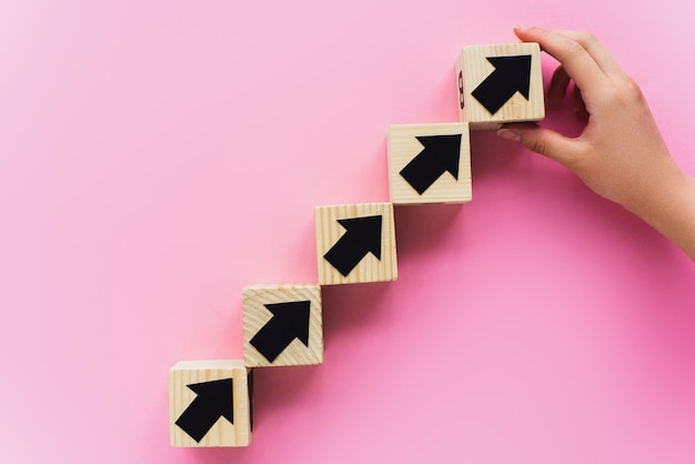 Partial view of hand near wooden blocks with black arrows on pink background business concept