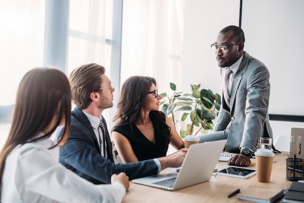 Partial view of multiracial group of business coworkers in formal wear discussing new business plan