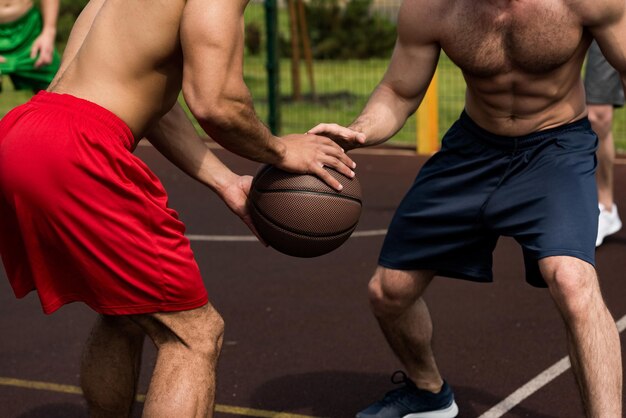 Photo partial view of shirtless sportsmen playing basketball at basketball court