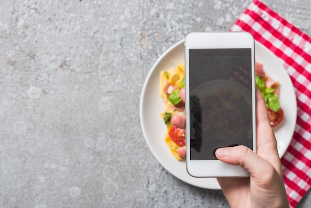 Partial view of woman taking picture of Pappardelle with tomatoes basil and prosciutto on